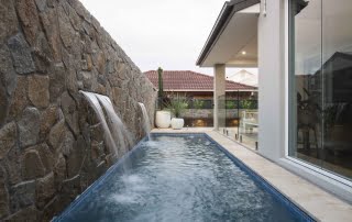 Coastal backyard pool with stone wall water feature