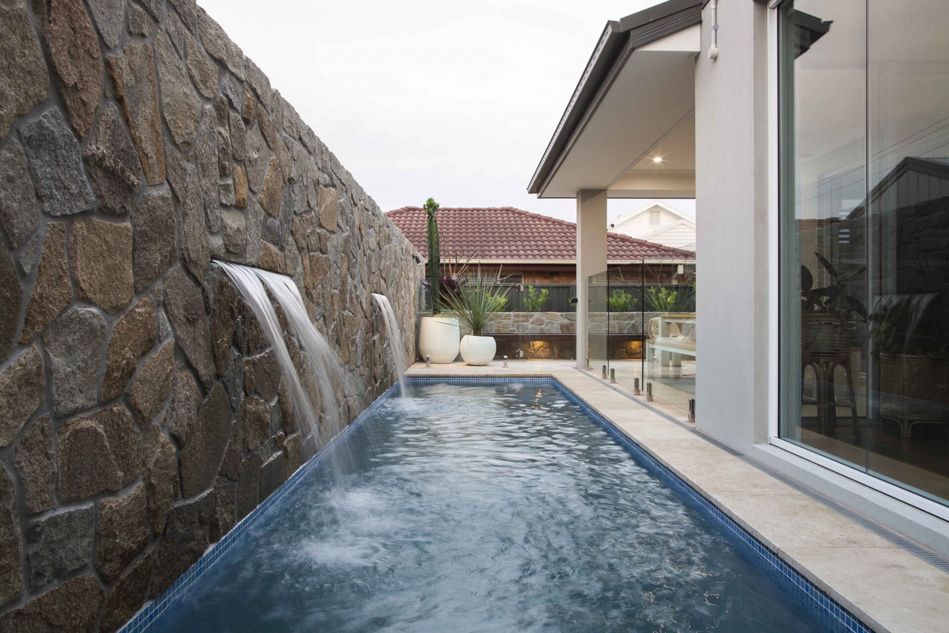 Coastal backyard pool with stone wall water feature